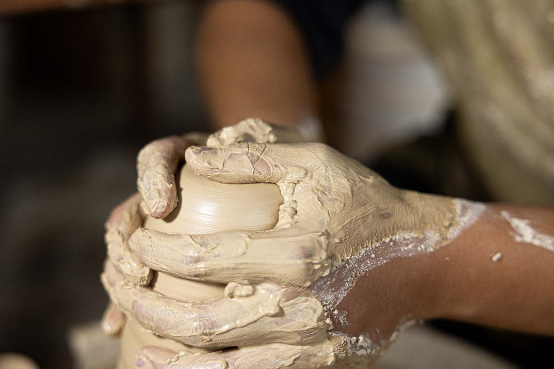Close-up view of a potter’s hands shaping clay on the wheel, highlighting the tactile quality and craftsmanship behind handmade vessels.