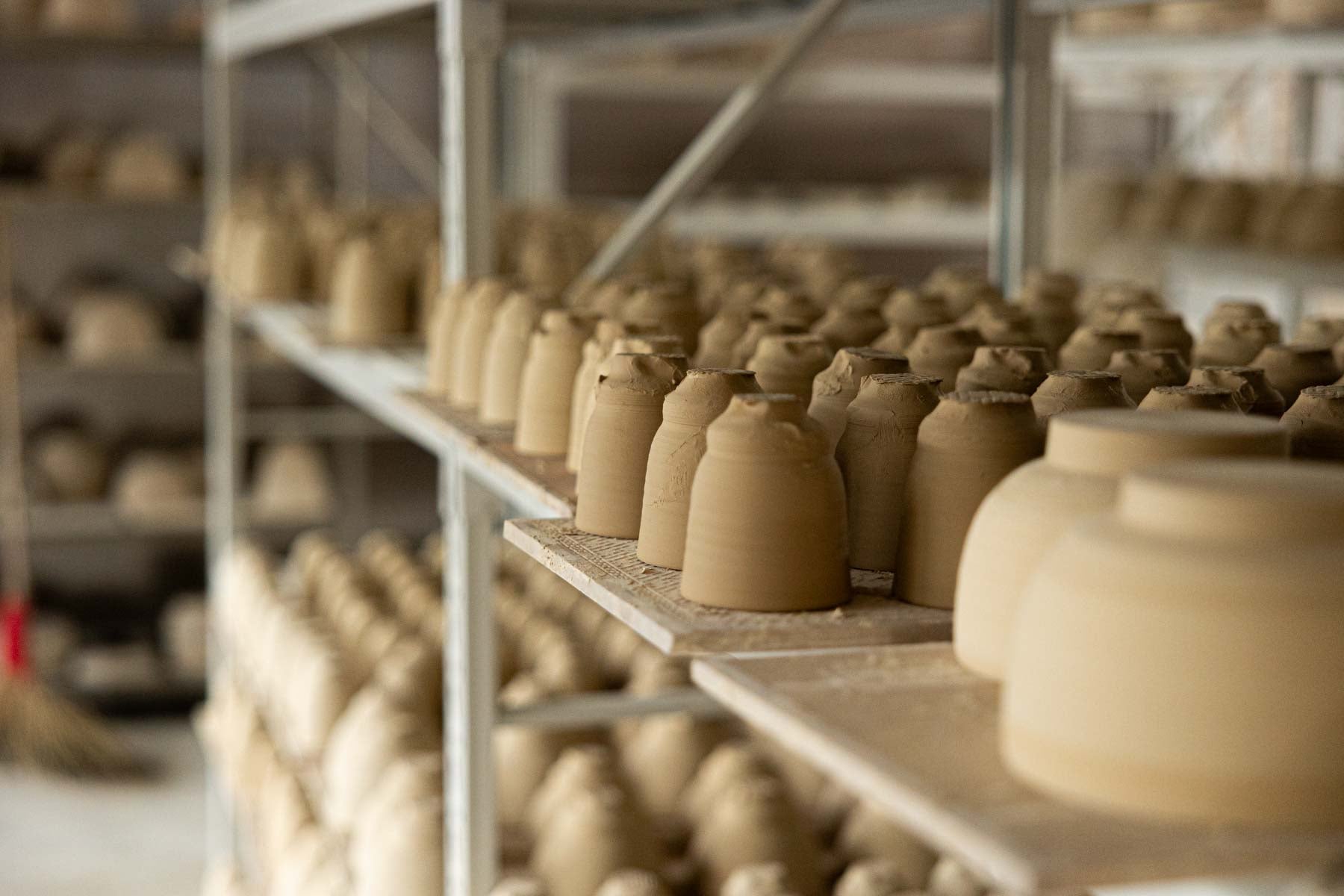 Shelves filled with freshly wheel-thrown clay cup bodies, showcasing the early stage of handmade vessel making