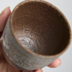 Close-up of handmade stoneware teacup showing textured iron clay body and soft white slip glaze contrast.