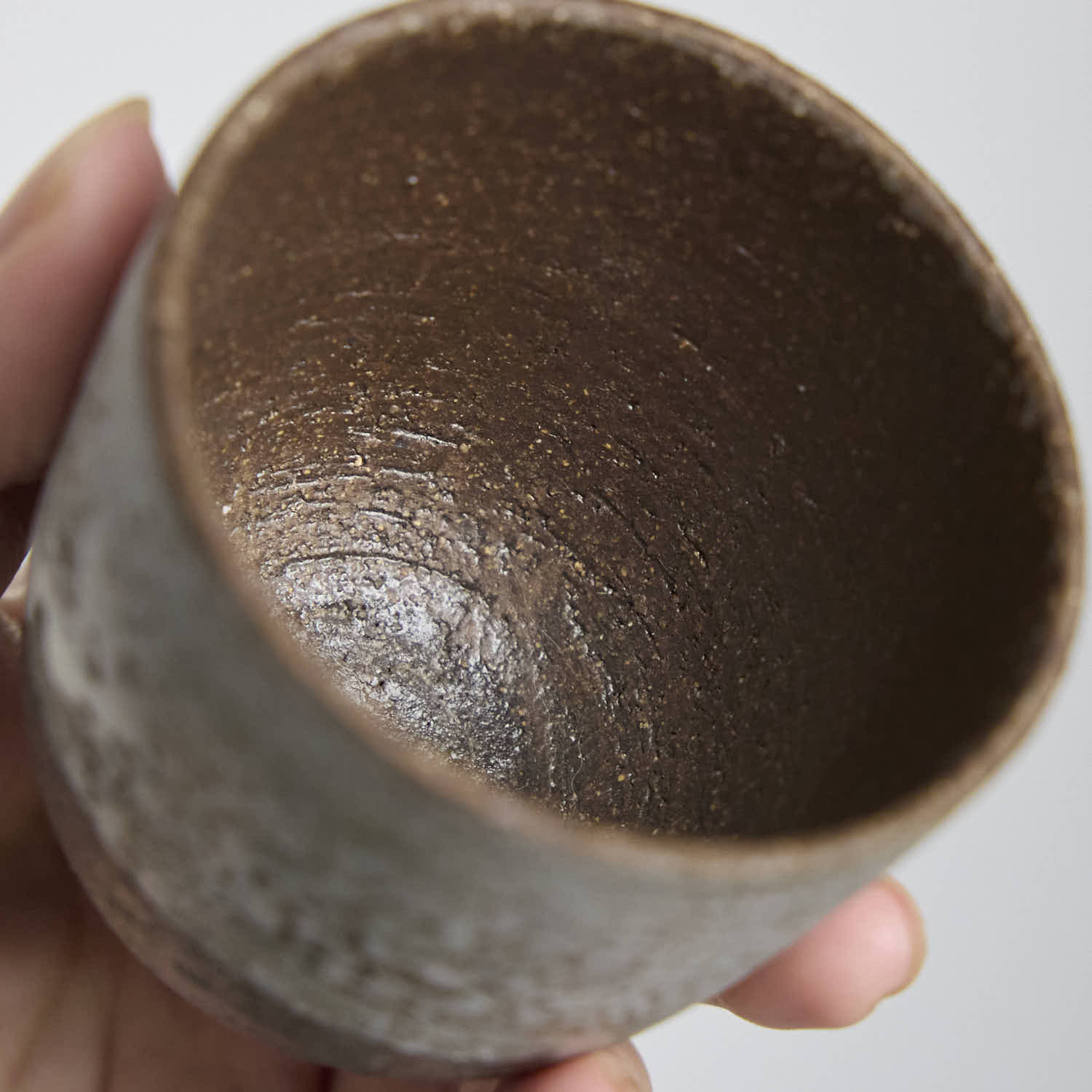 Close-up of handmade stoneware teacup showing textured iron clay body and soft white slip glaze contrast.