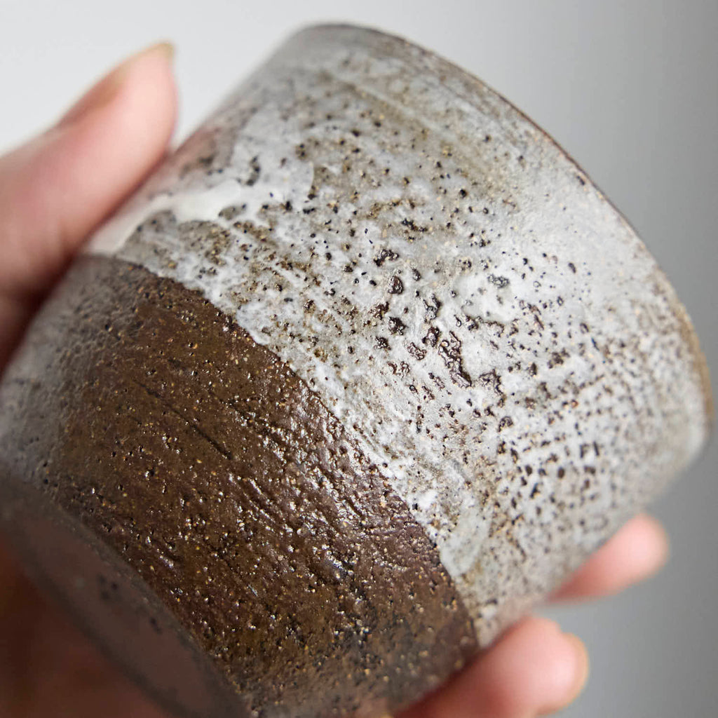 Close-up of handmade stoneware teacup showing textured iron clay body and soft white slip glaze contrast.