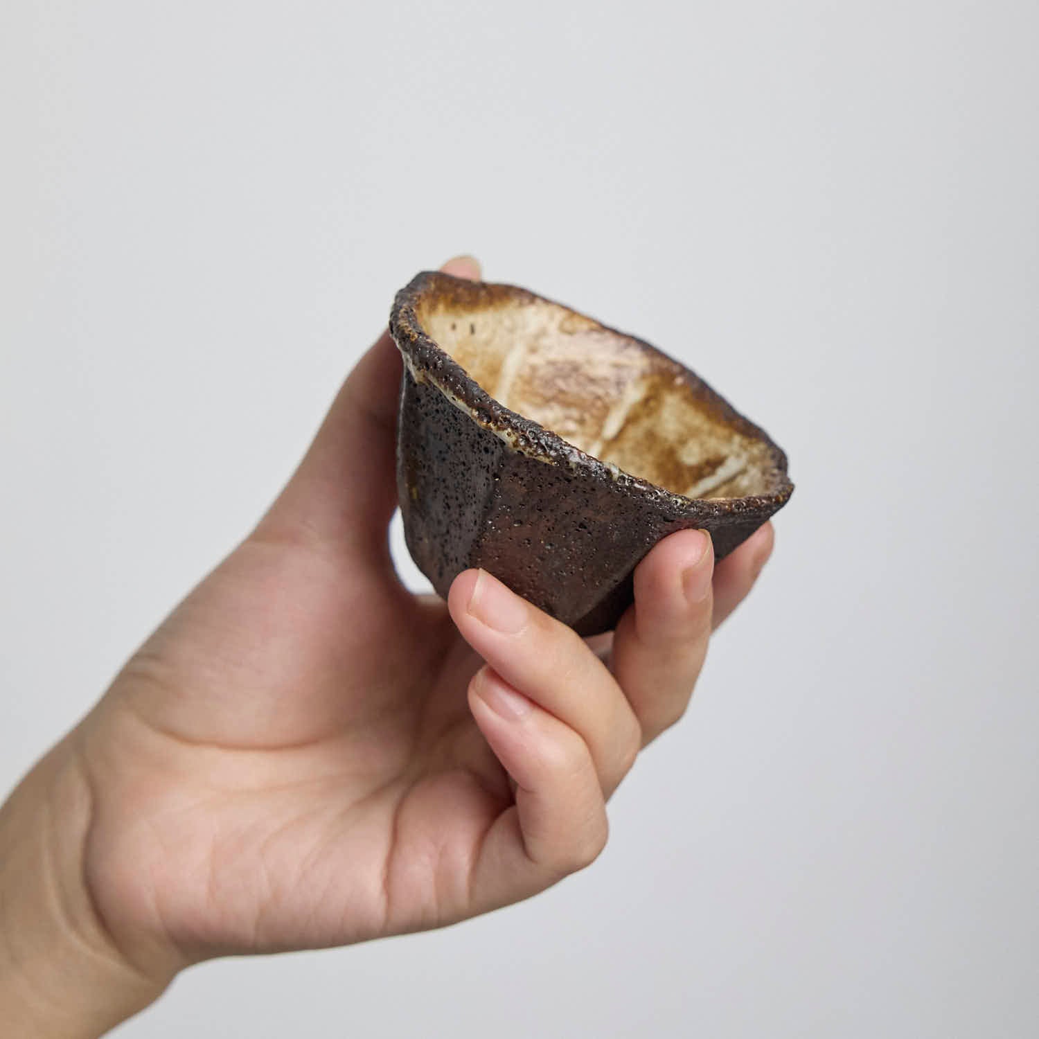 Handbuilt wood-fired clay cup with white slip finish, wabi-sabi style ceramic teacup showing natural ash glaze and irregular rim.