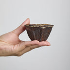 Handbuilt wood-fired clay cup with white slip finish, wabi-sabi style ceramic teacup showing natural ash glaze and irregular rim.