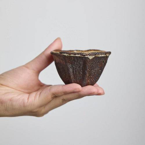 Handbuilt wood-fired clay cup with white slip finish, wabi-sabi style ceramic teacup showing natural ash glaze and irregular rim.