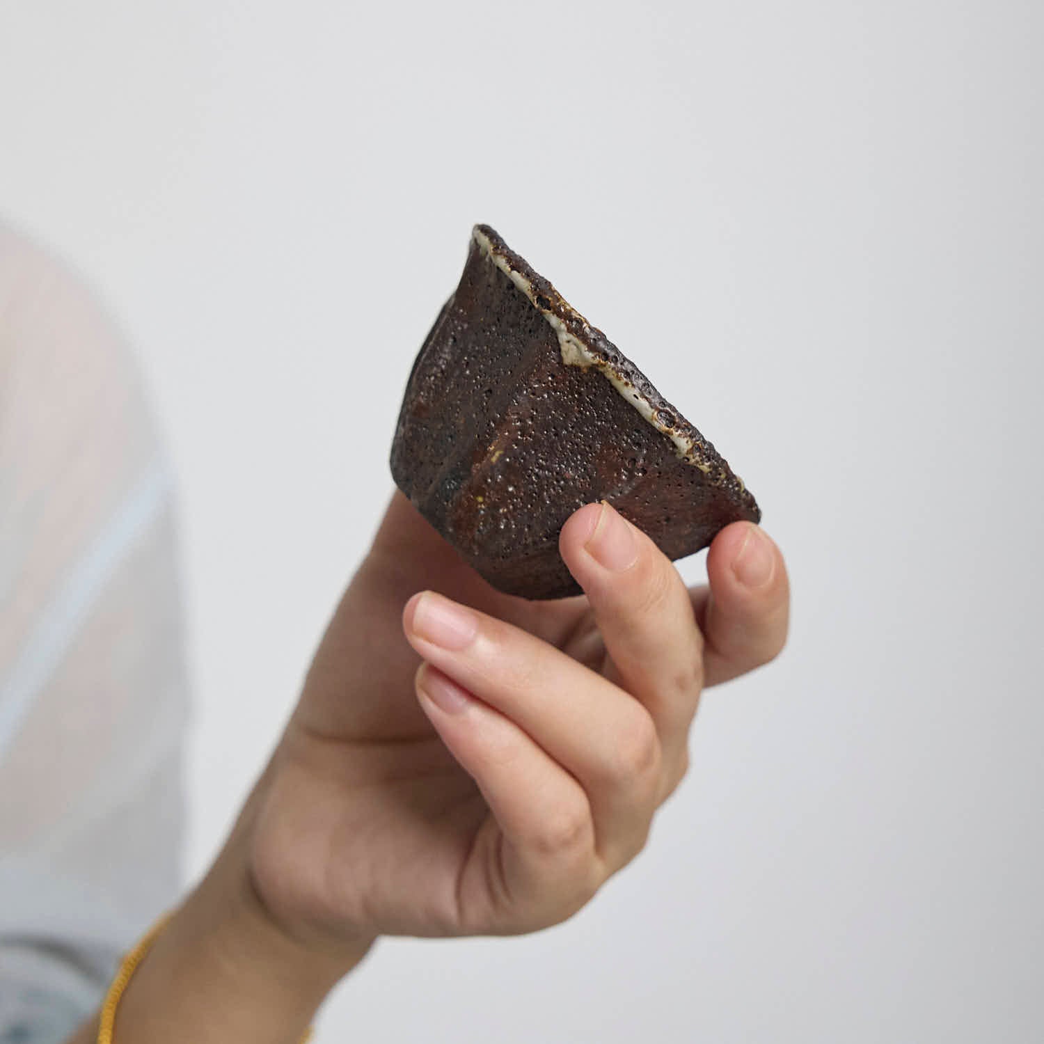 Handbuilt wood-fired clay cup with white slip finish, wabi-sabi style ceramic teacup showing natural ash glaze and irregular rim.