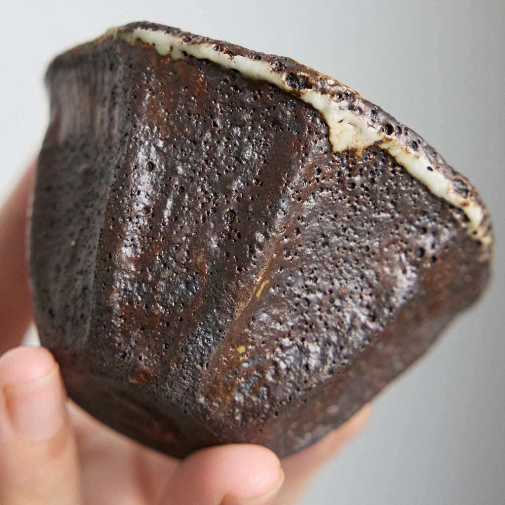 Handbuilt wood-fired clay cup with white slip finish, wabi-sabi style ceramic teacup showing natural ash glaze and irregular rim.