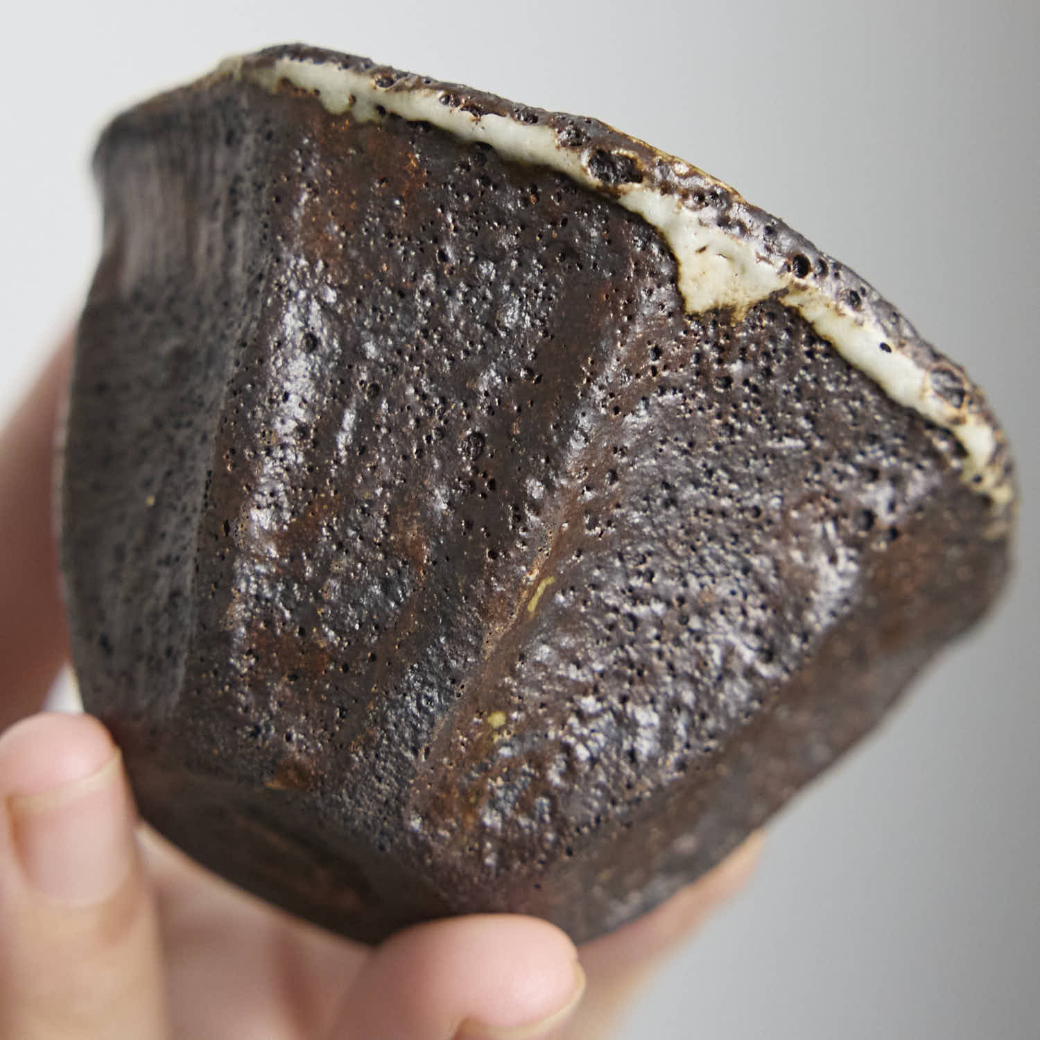 Handbuilt wood-fired clay cup with white slip finish, wabi-sabi style ceramic teacup showing natural ash glaze and irregular rim.