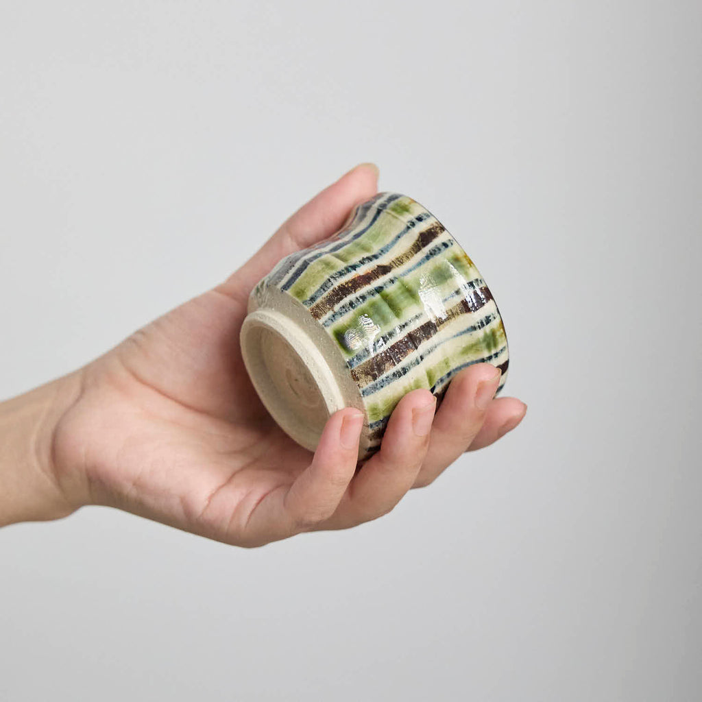 Hand-pinched crackle glaze tea cup with striped decoration on a wooden table.