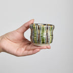 Hand-pinched crackle glaze tea cup with striped decoration on a wooden table.