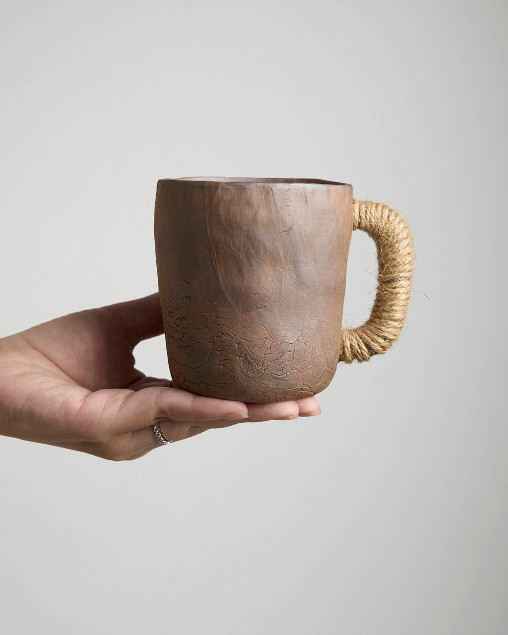 Hand-pinched rustic stoneware mug in earth tones with hemp-wrapped handle