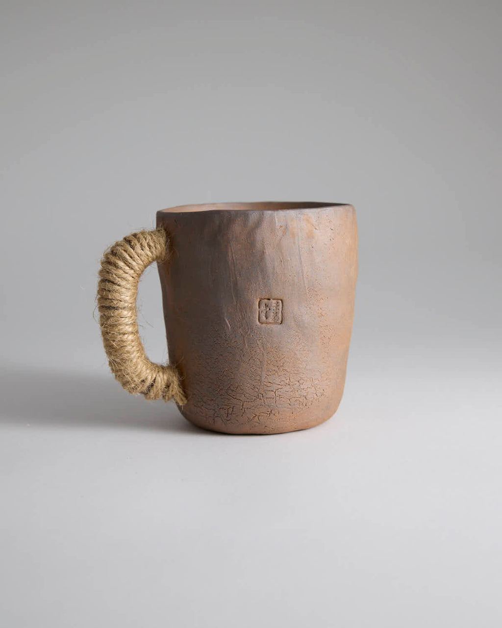 Hand-pinched rustic stoneware mug in earth tones with hemp-wrapped handle