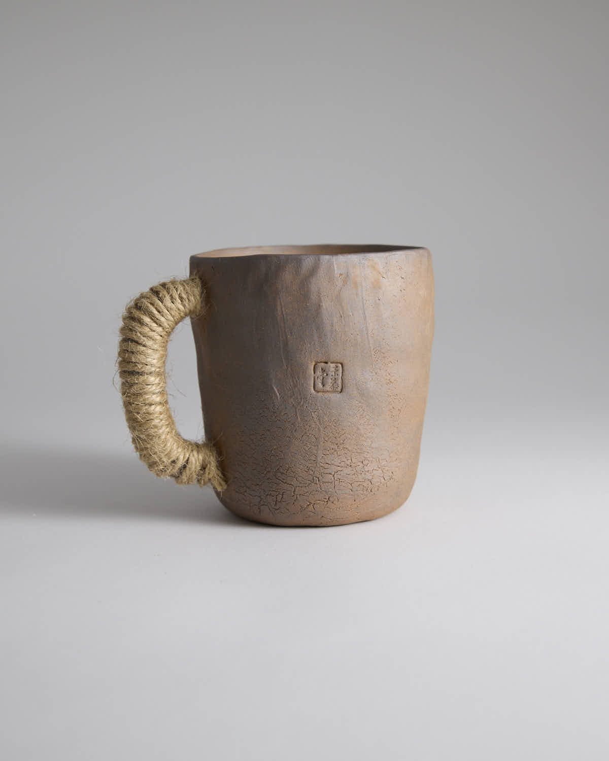 Hand-pinched rustic stoneware mug in earth tones with hemp-wrapped handle