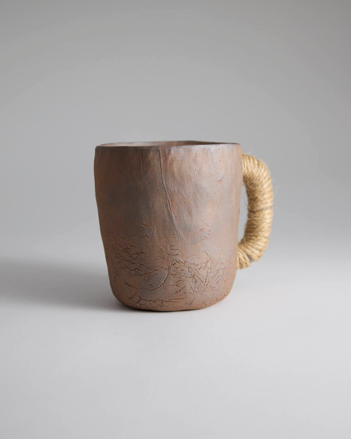 Hand-pinched rustic stoneware mug in earth tones with hemp-wrapped handle