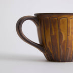 Rustic stoneware coffee cup and saucer set with textured surface inspired by Egyptian motifs