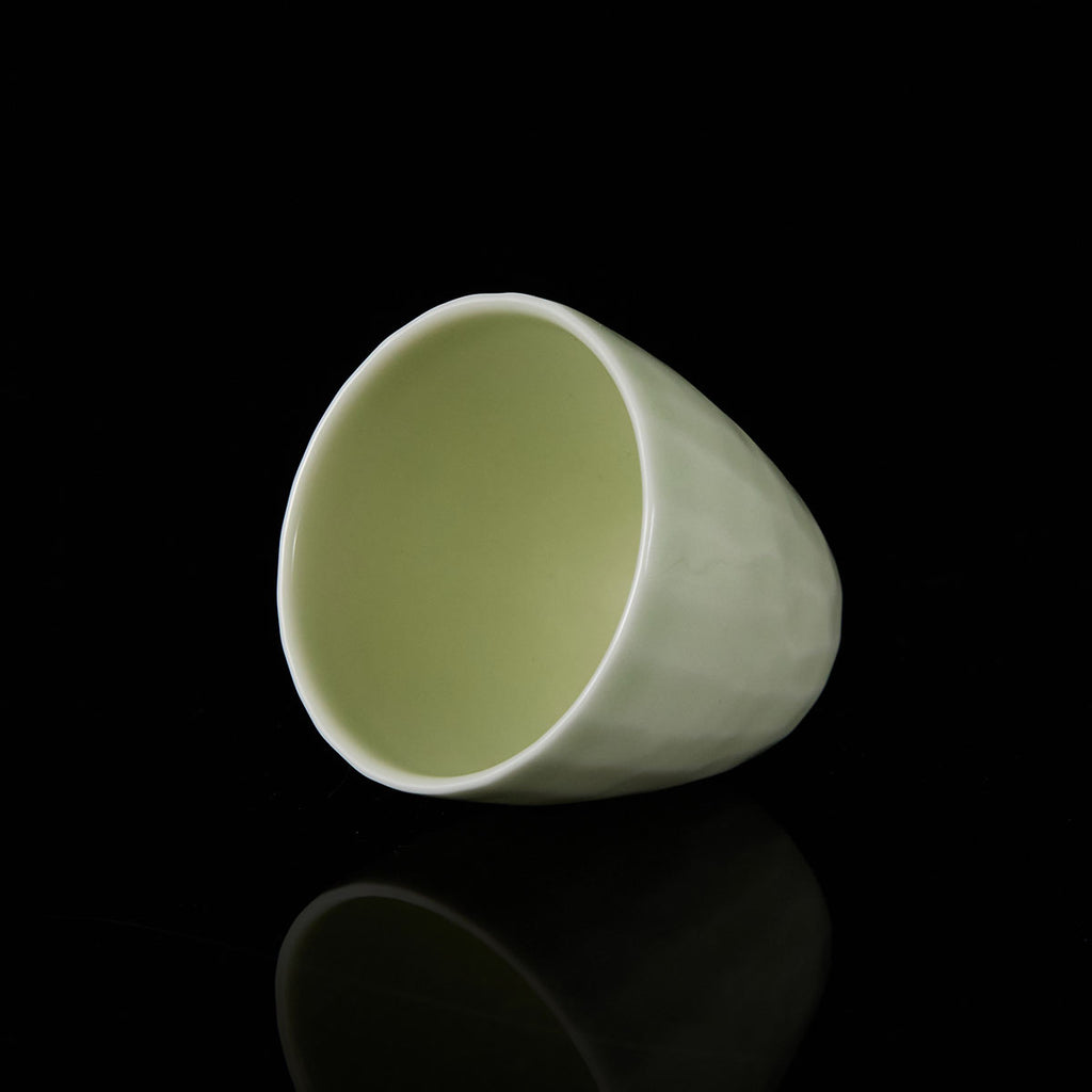 Ou Kiln hammered-texture celadon teacup with a tapered shape and soft jade-like glaze on a black background.