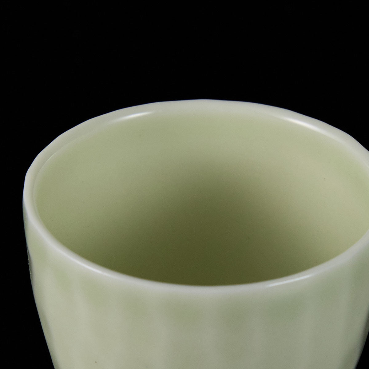 Ou Kiln hammered-texture celadon teacup with a tapered shape and soft jade-like glaze on a black background.