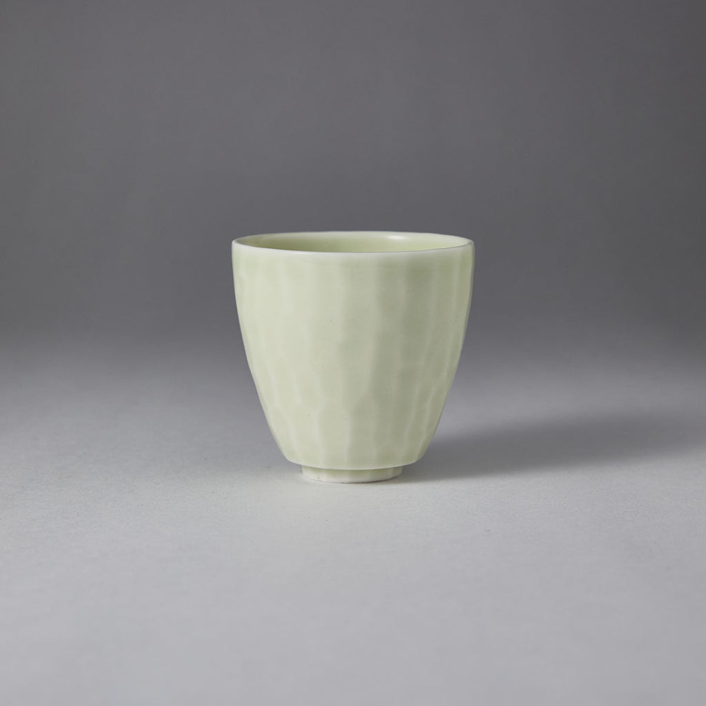 Ou Kiln hammered-texture celadon teacup with a tapered shape and soft jade-like glaze on a black background.
