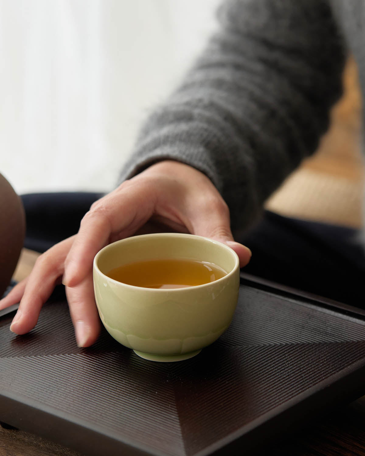 hand holding ou ware celadon lotus petal teacup with tea handmade gongfu tea cup for steeping